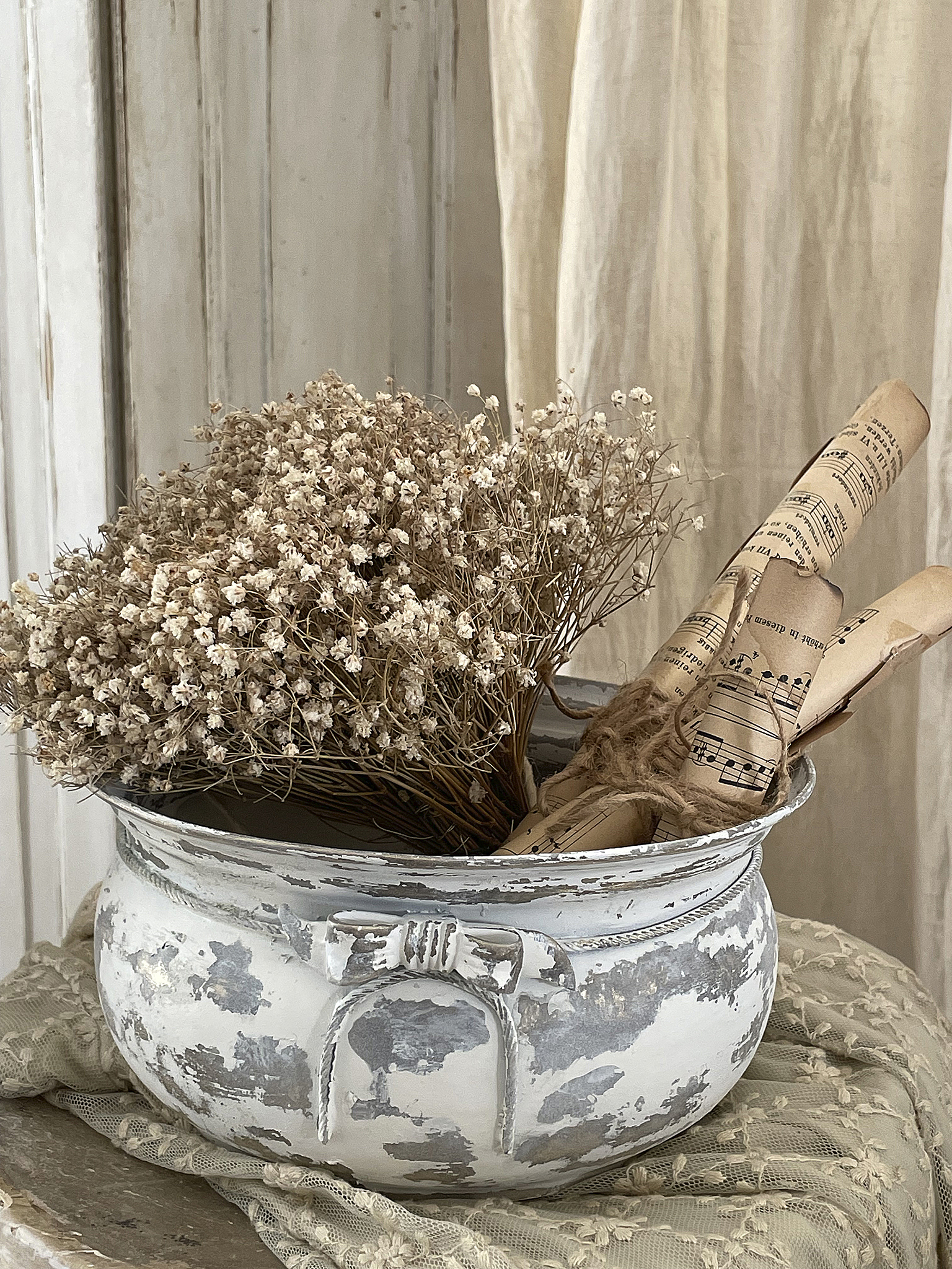 Eleganter Blumentopf mit braunen getrockneten Blumen und alten Notenrollen auf einem Tisch