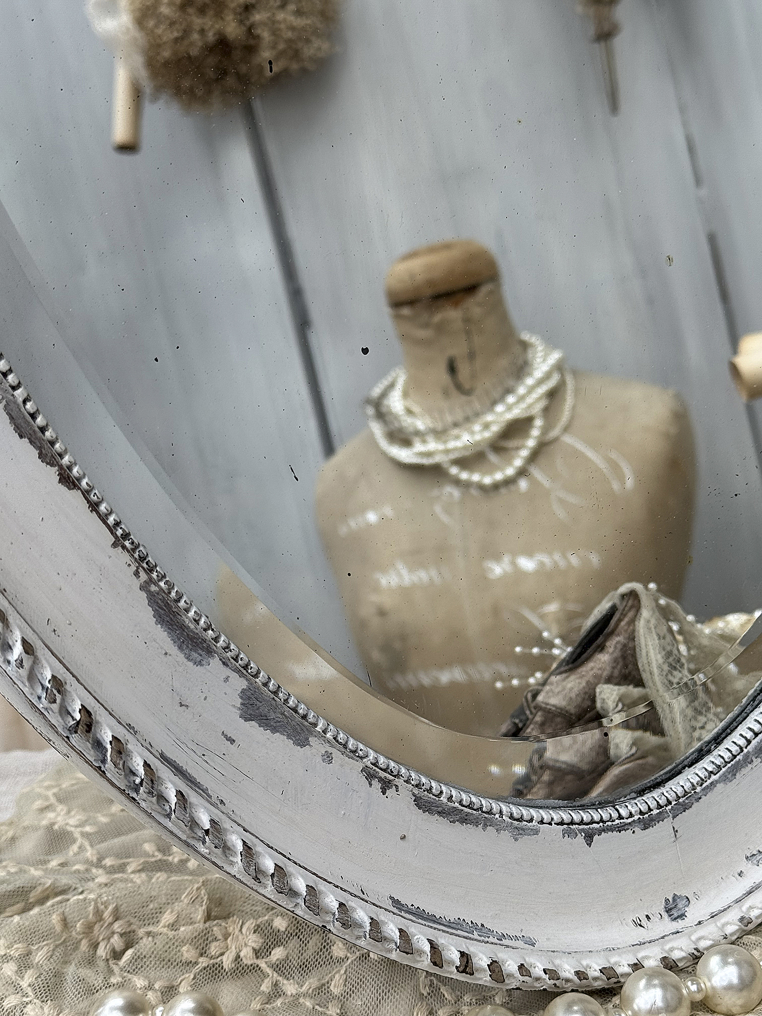 Detailaufnahme eines vintage Spiegels, der ein Mannequin mit Perlenschmuck reflektiert.