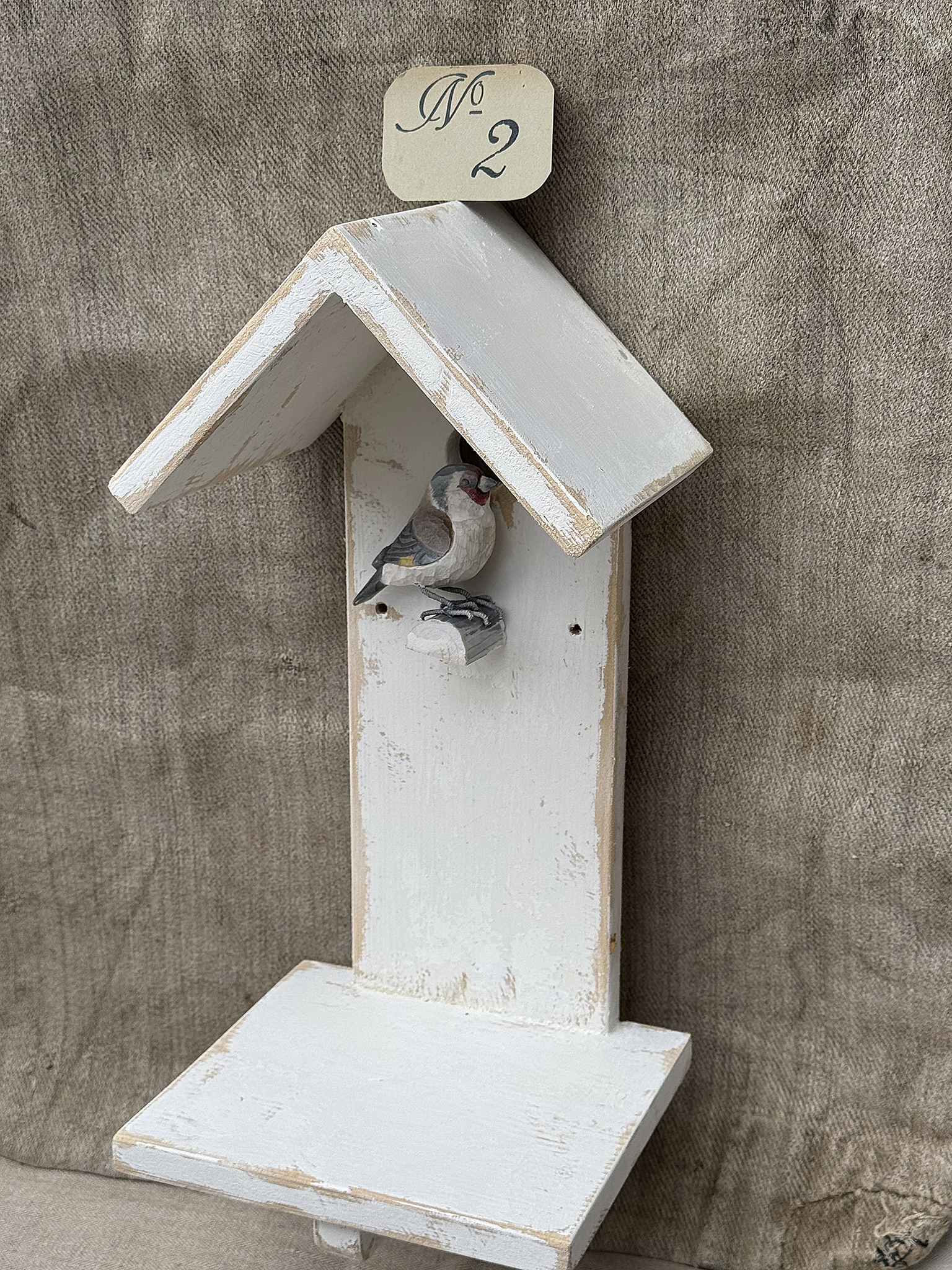 Hölzernes Vogelhaus mit einer kleinen Vogelverzierung und einem Schild mit der Nummer 2