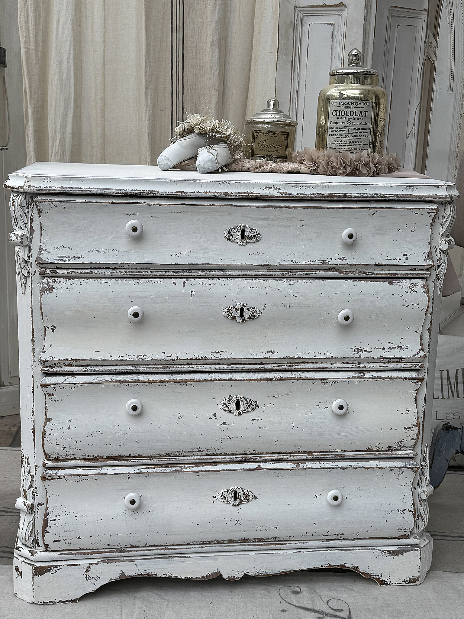 Weiße vintage Kommode im Shabby-Chic-Stil mit dekorativen Details und vier Schubladen.